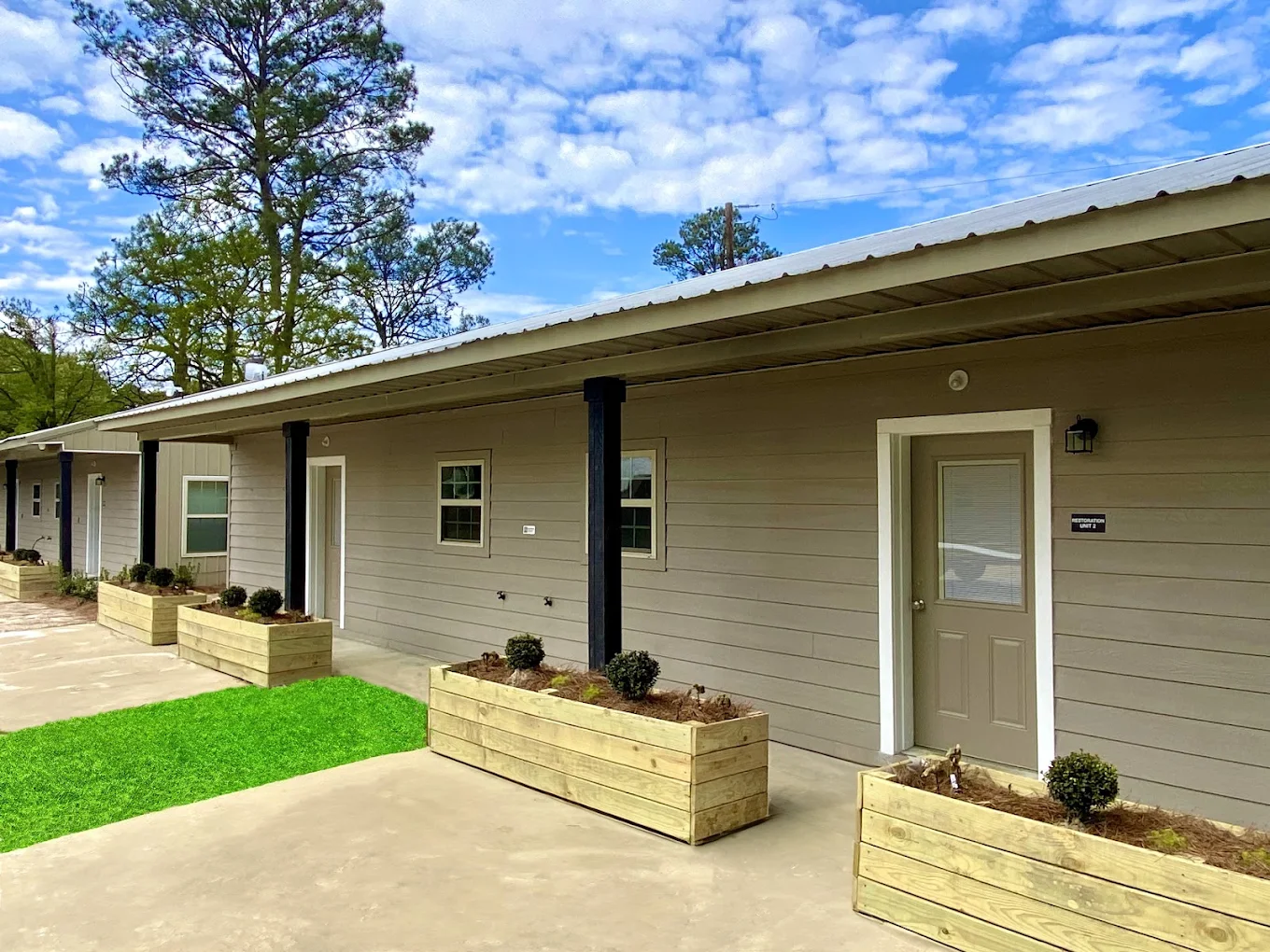 Exterior view of the Freedom Recovery facility in West Monroe with covered walkways, landscaped planter boxes, and surrounding pine trees