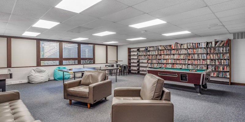 Spacious recreational room with cozy seating, a large bookshelf, pool table, bean bags, and ping pong area, creating a relaxed and inviting space.