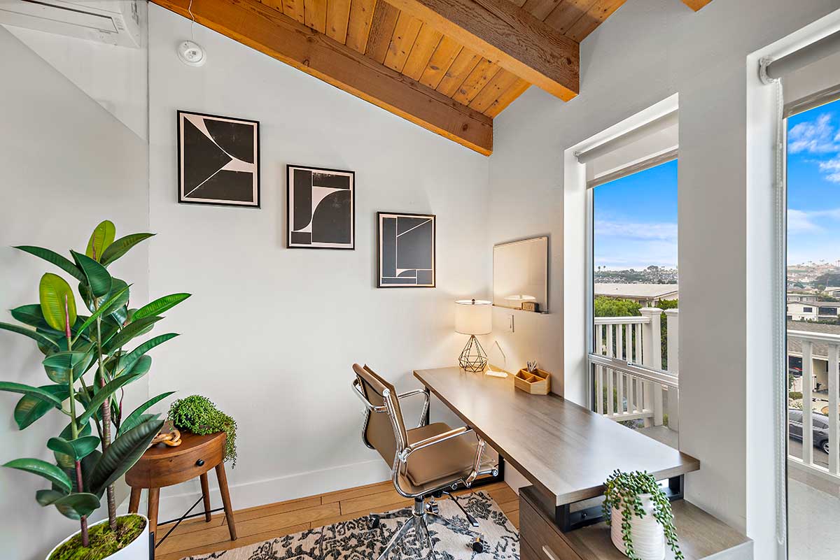 Private study with wood desk, office chair, plants, abstract wall art, and large windows overlooking the neighborhood
