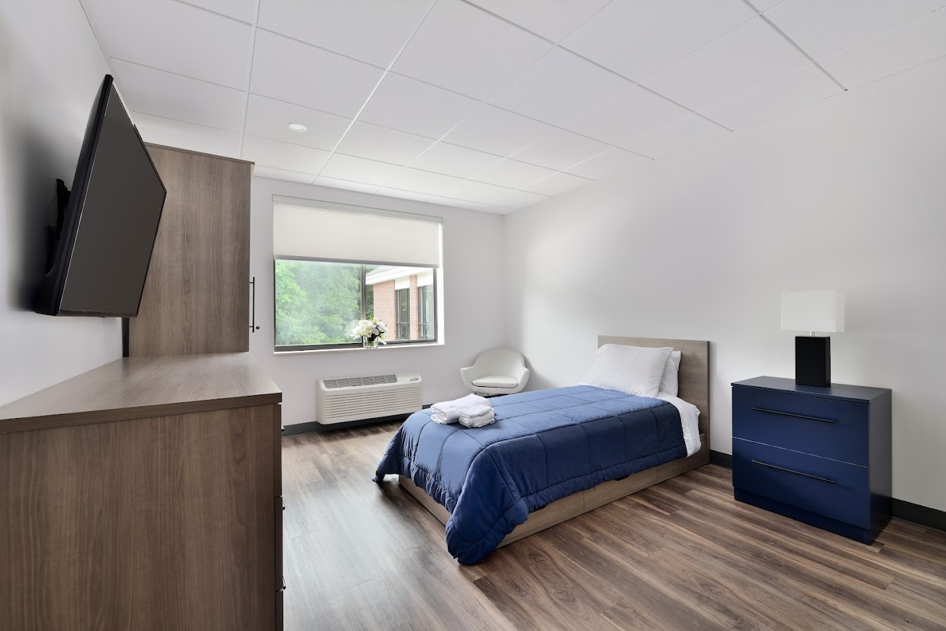 A clean bedroom with a blue comforter and TV.