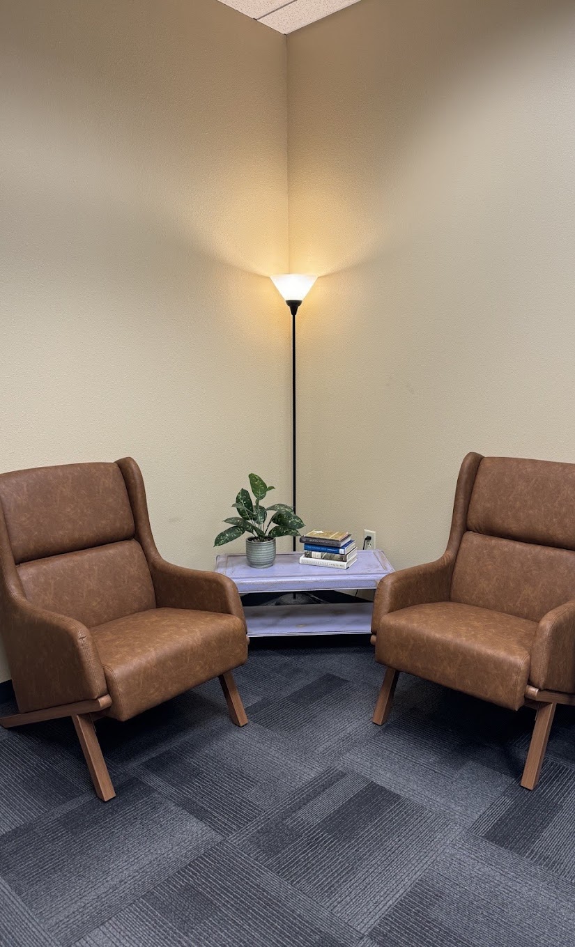 Two brown chairs with a small table and lamp in corner counseling space