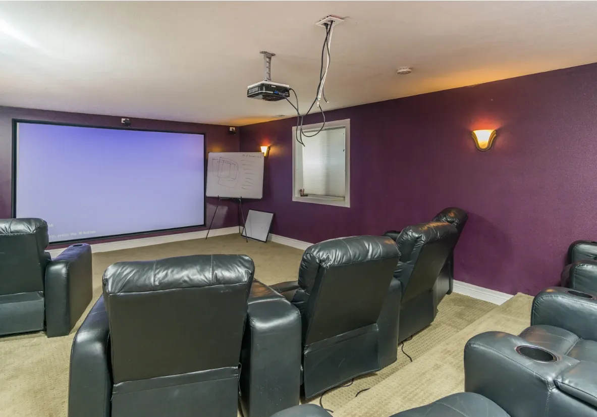 Cozy media room with black leather recliners, large projector screen, purple walls, and ceiling-mounted projector