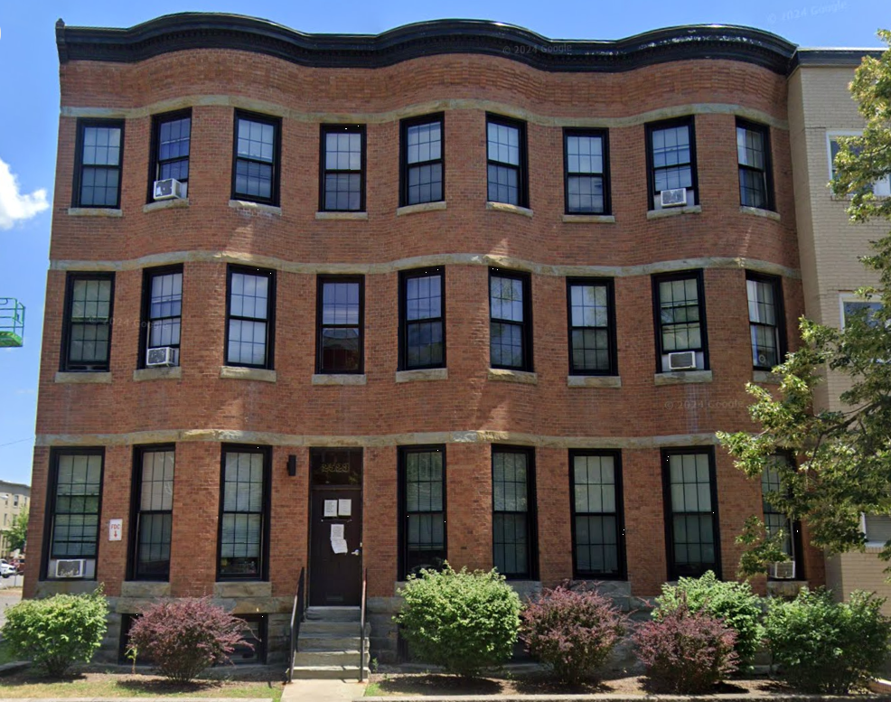 Three-story brick building with black-framed windows and shrubs in front