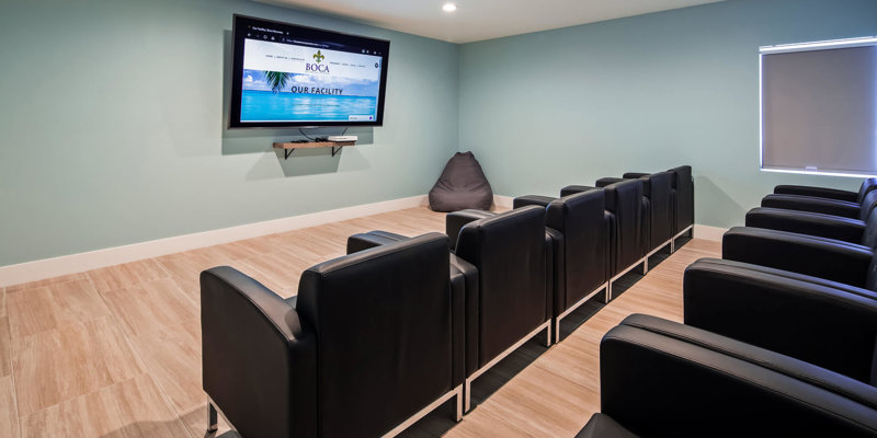 A cozy and modern theater room with comfortable black chairs, a large screen, and soft lighting, providing a relaxing space for entertainment or presentations.