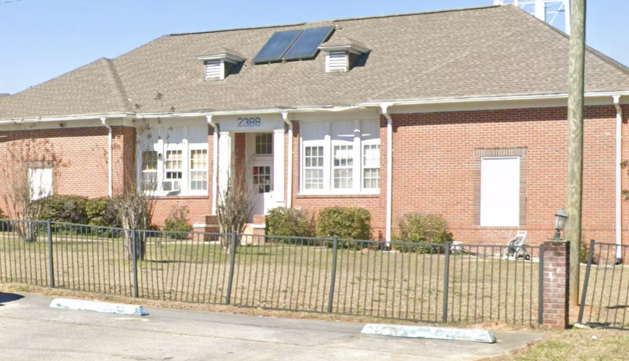 Red brick facility building with white windows and fenced lawn