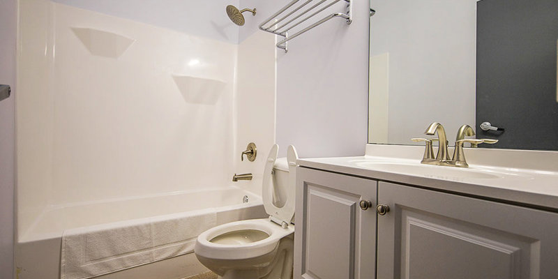 A clean, well-lit bathroom featuring a white bathtub, vanity, and toilet. The space includes chrome fixtures and ample counter space.