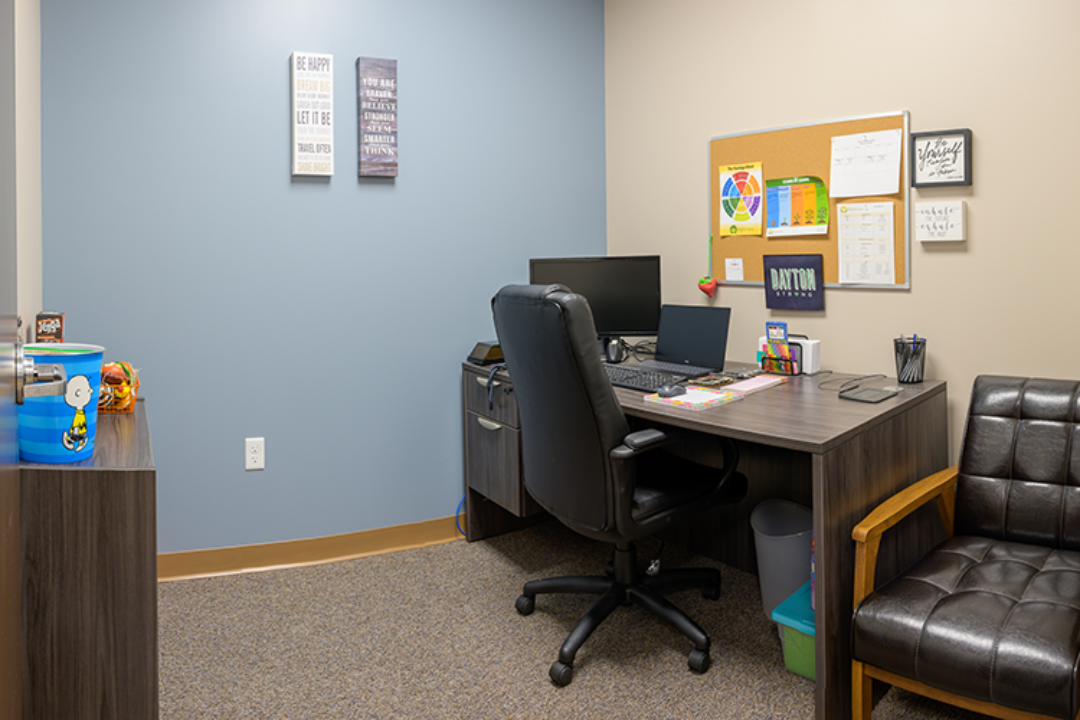Private consultation office with desk, computer, visitor chair, and blue accent wall