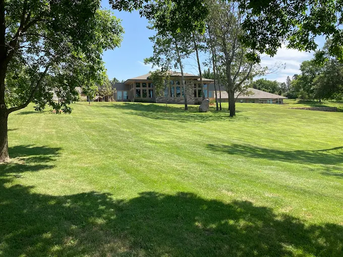 Large grassy lawn with trees and facility in background