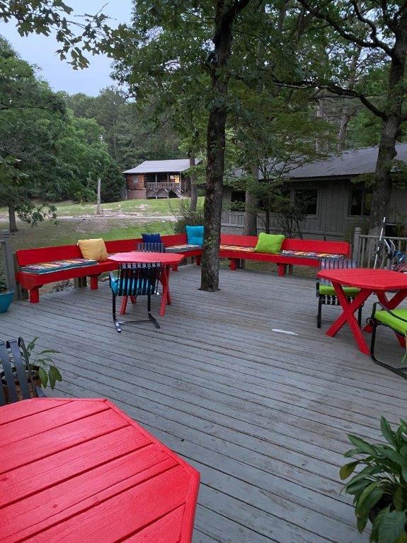 Patio with bright red tables, benches, and multicolored cushions in a wooded setting.