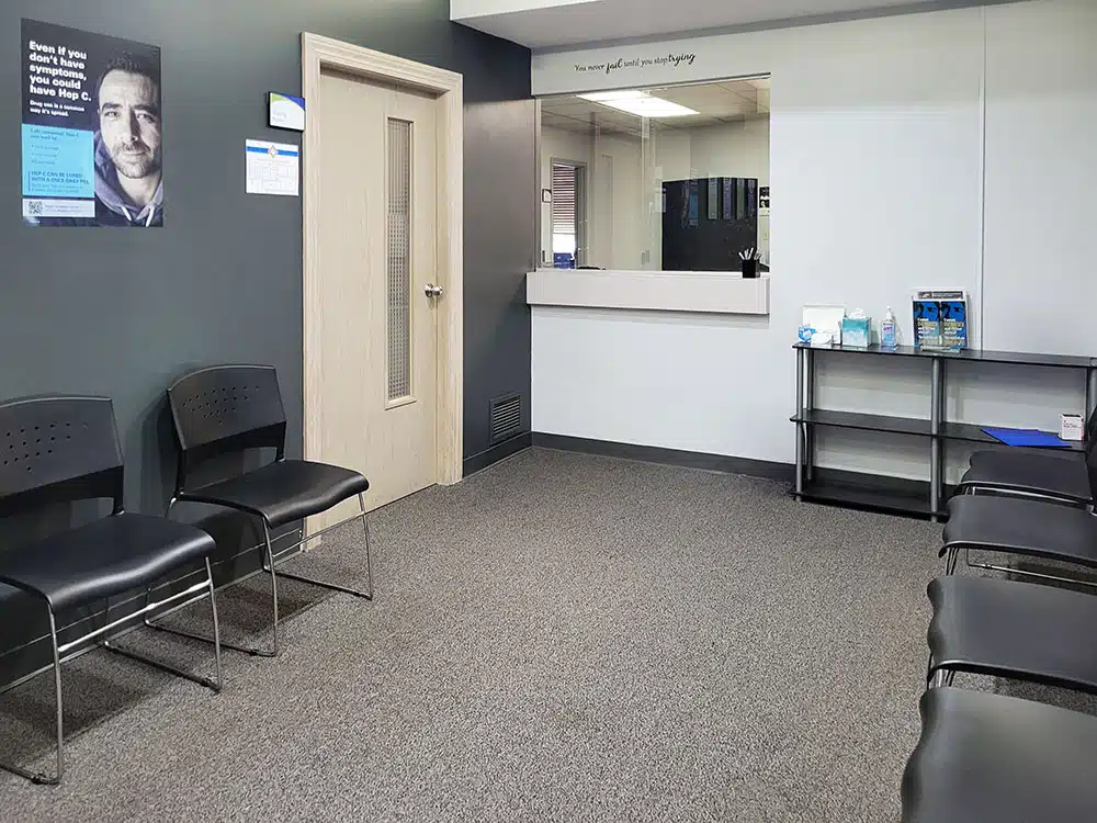 Waiting room with chairs along walls, reception window, and doorway leading to interior offices