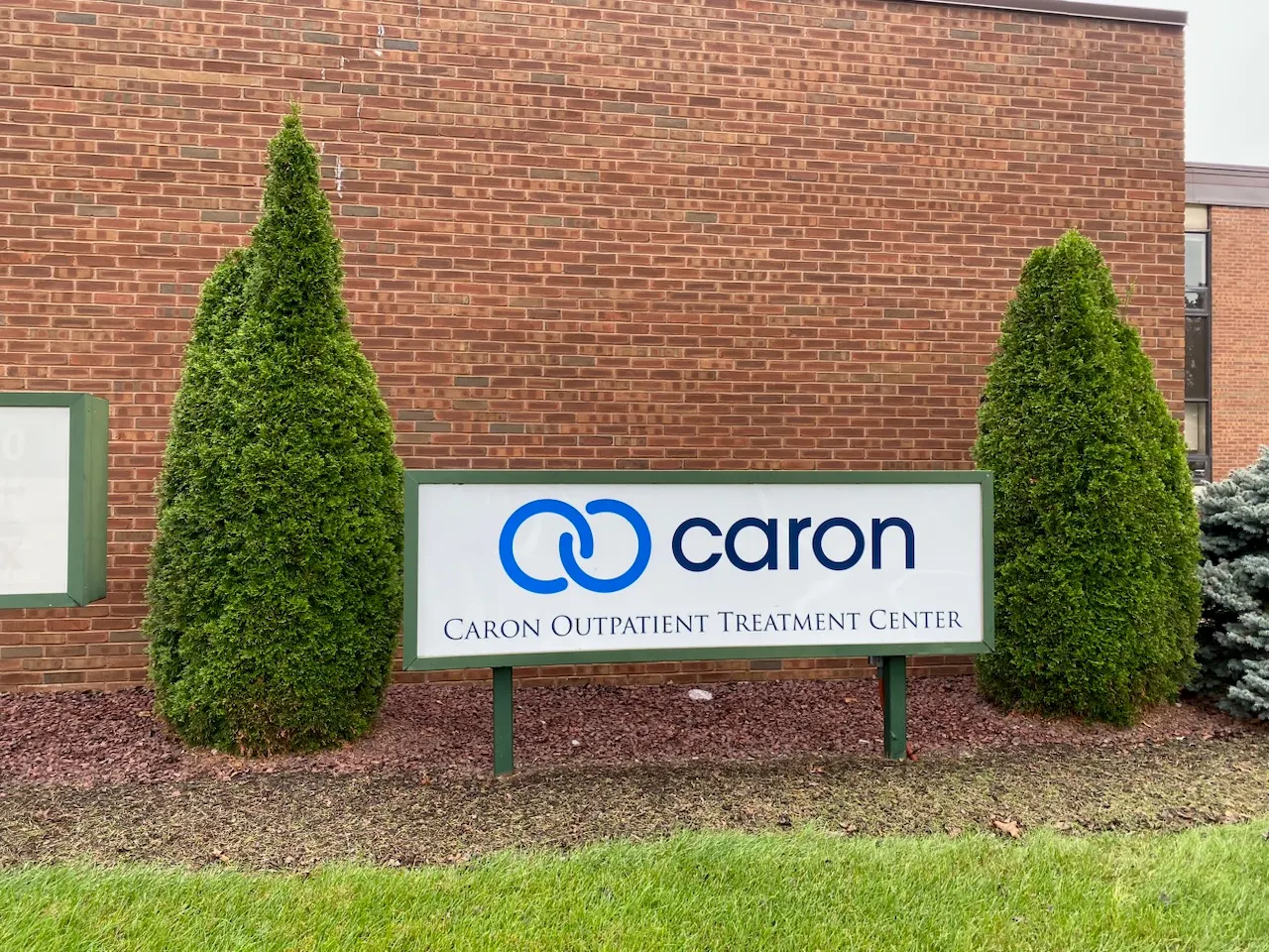 Caron Outpatient Treatment Center sign between landscaped shrubs outside a brick building