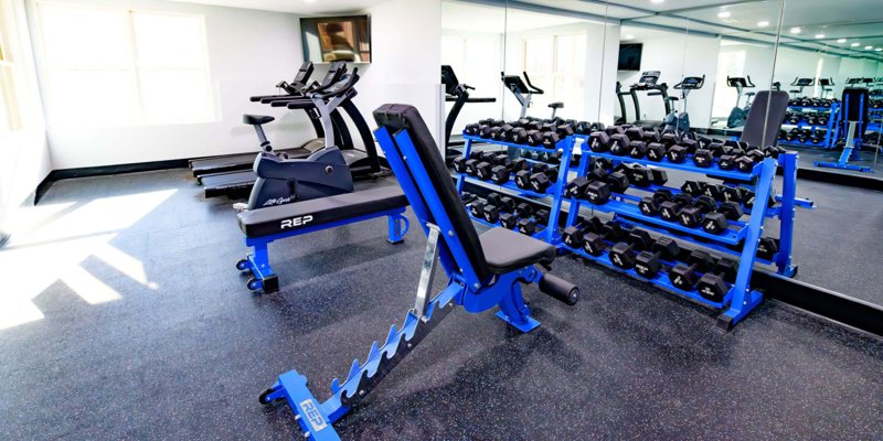 Well-equipped fitness room at Boca Recovery Center featuring cardio machines, free weights, and benches, creating an inviting space for exercise.