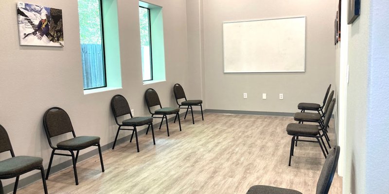 A bright group therapy room with chairs arranged in a circle, featuring a whiteboard and natural light from large windows, fostering openness.