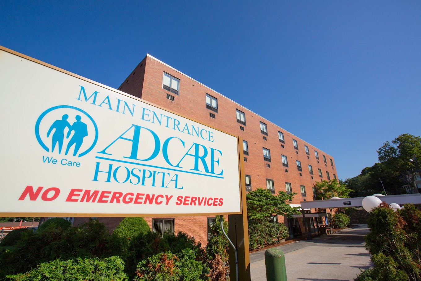 The entrance of AdCare Hospital with a sign and red brick exterior.