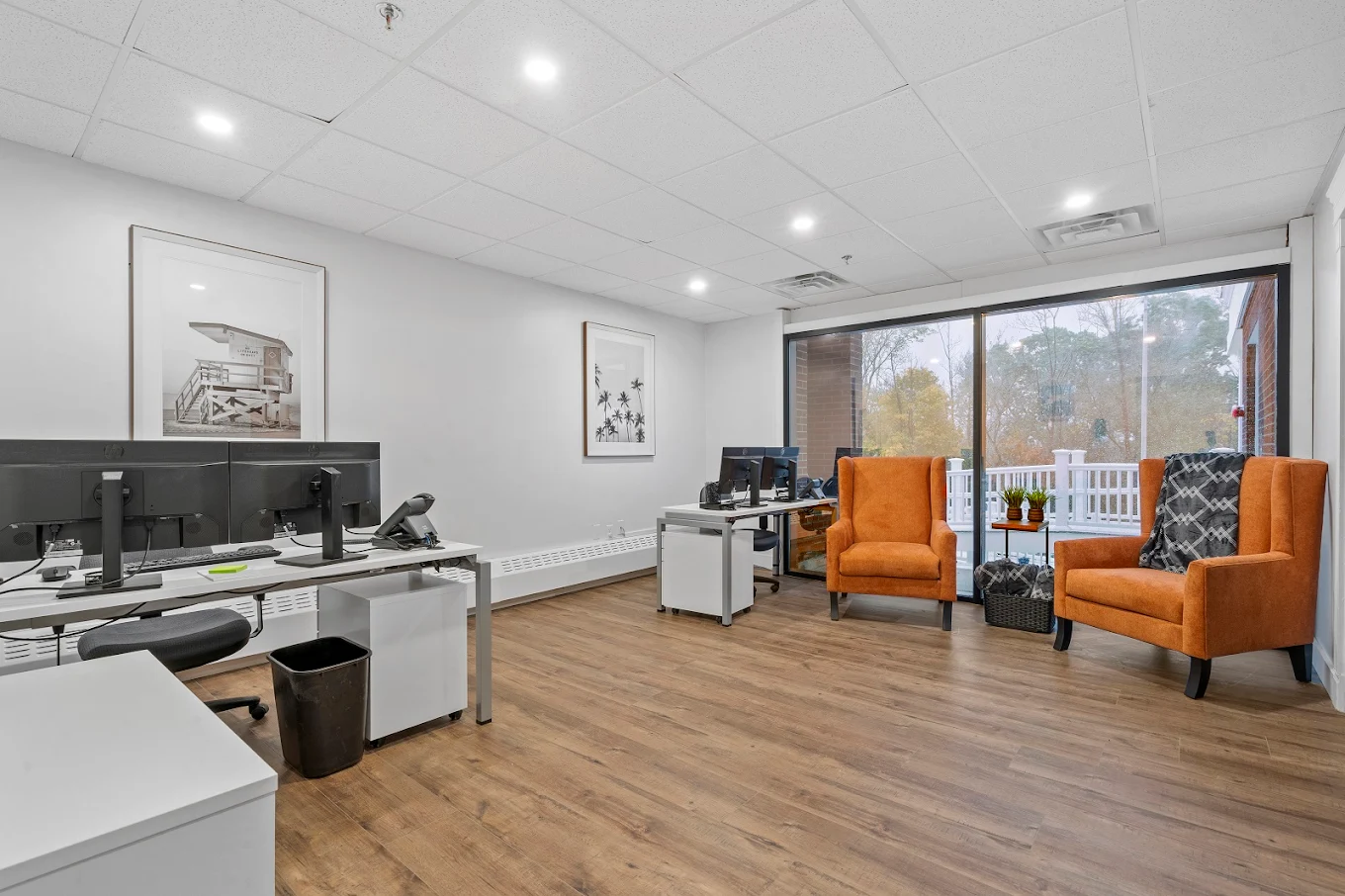 Modern admissions office with dual workstations, orange armchairs, and large window view to outdoor patio