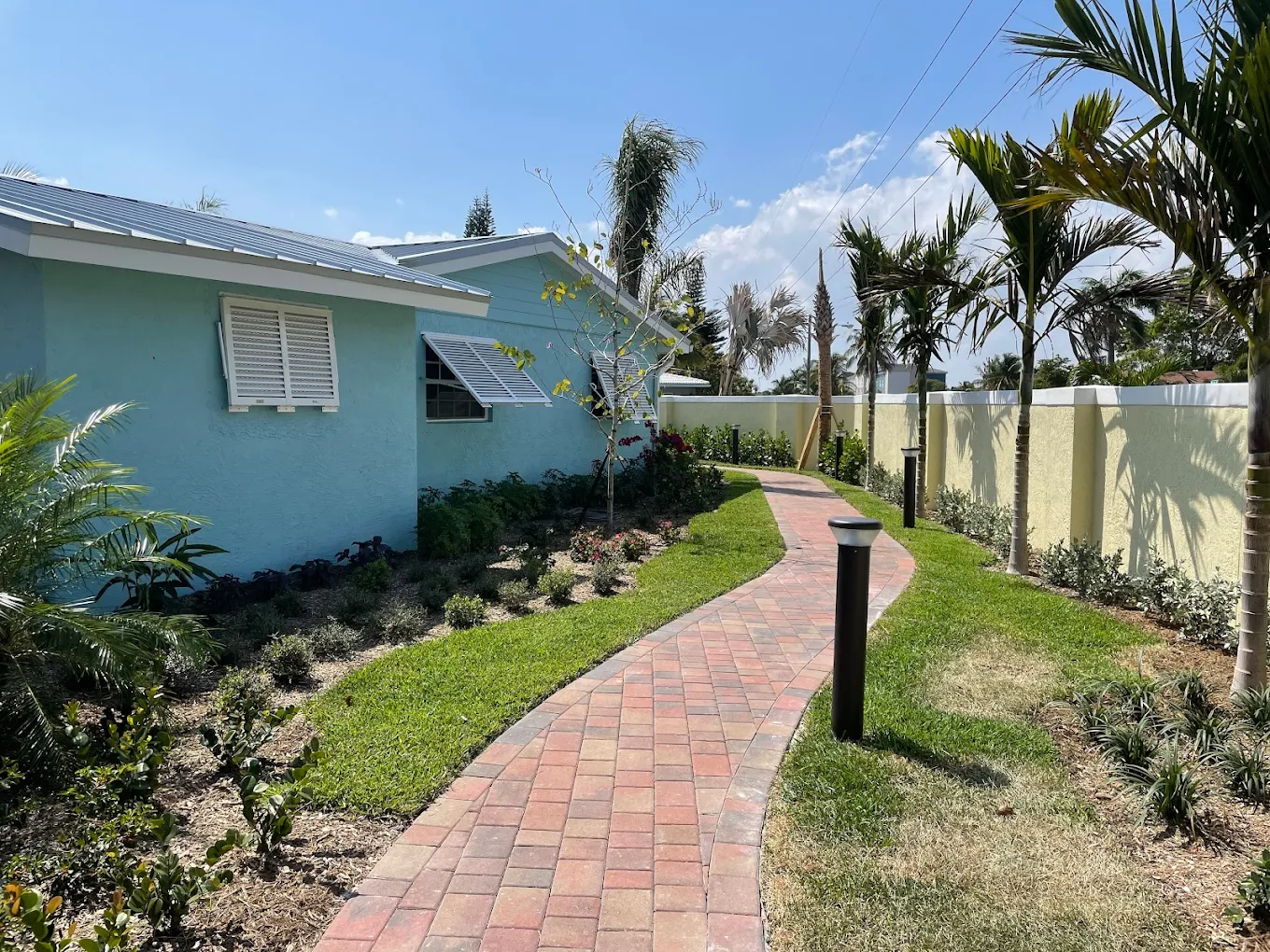 Brick pathway beside blue building lined with palm trees