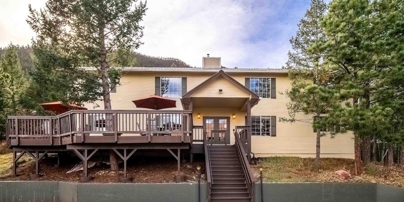 A welcoming two-story house with a large wooden deck, surrounded by trees and nature, offering a peaceful, retreat-like atmosphere.