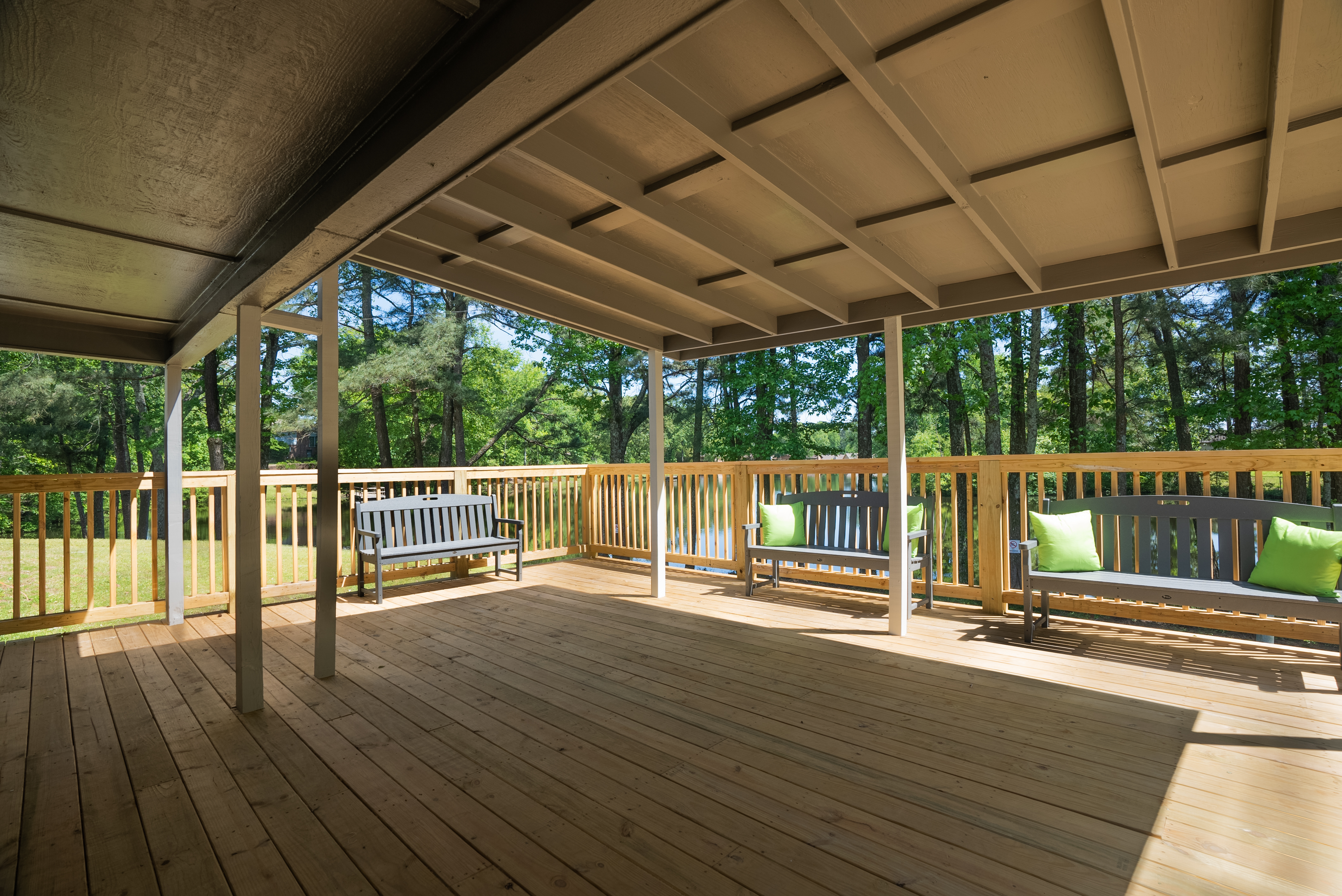 Spacious covered deck with benches overlooking trees.