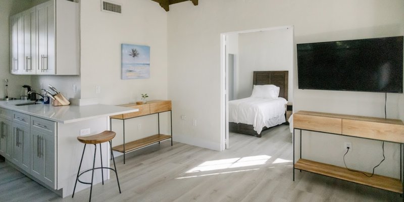 A bright, modern living space with wooden beams, a cozy kitchenette, and a bedroom featuring a comfortable bed. The room feels airy and welcoming.