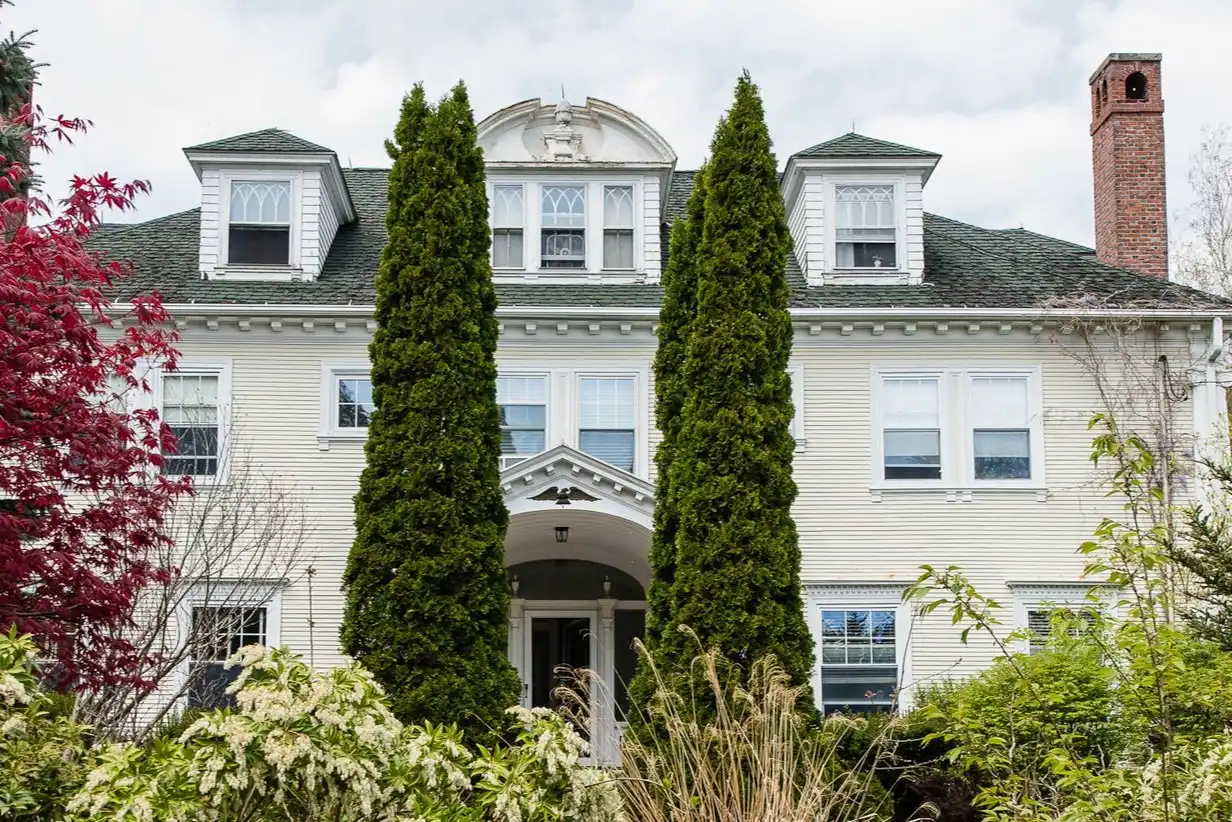 Large white home with tall trees and landscaped front entry