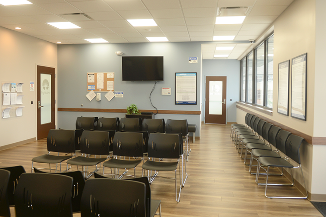 BrightView Health waiting area with rows of black chairs, wall-mounted television, large windows, informational displays, and wood-look flooring