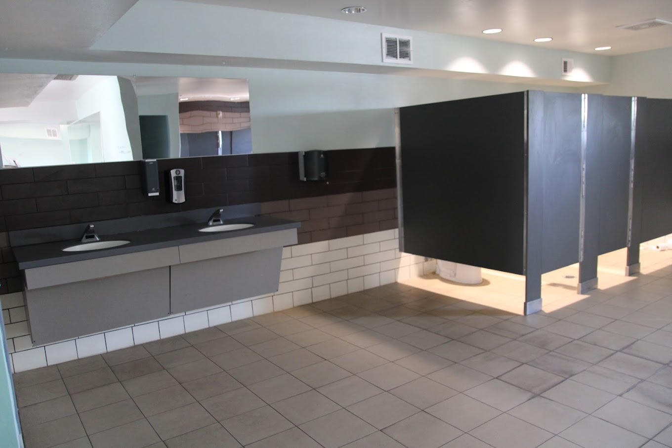  Modern restroom with sinks, mirror, and toilet stalls