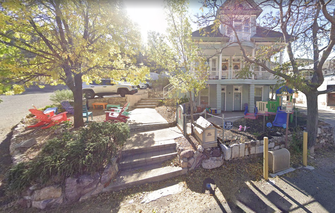Front yard with colorful outdoor chairs, steps leading to the entrance, and a fenced children's play area beside the building.