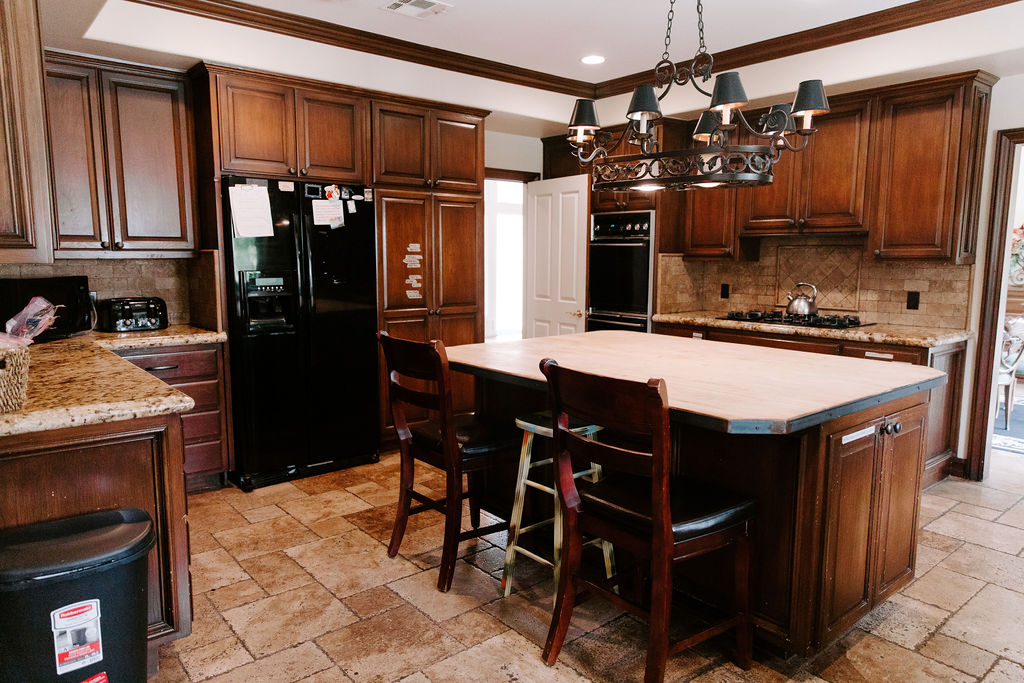 Traditional-style kitchen with dark wood cabinets, black appliances, granite countertops, and a large central island with seating