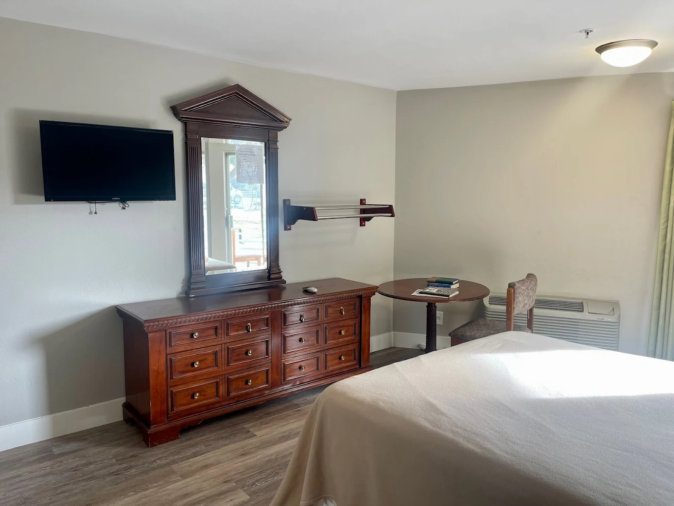 Cozy private bedroom with dresser, TV, table, and natural lighting.
