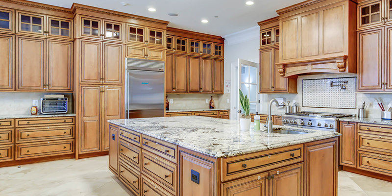 A spacious, luxurious kitchen with warm wooden cabinetry, a large marble island, stainless steel appliances, and modern lighting fixtures.