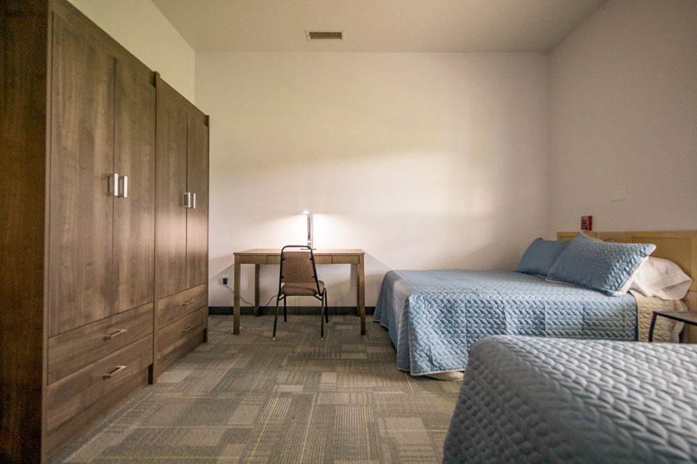 A bedroom with two beds, a desk, and a large wooden wardrobe.