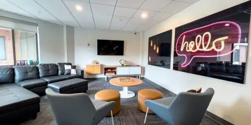  Cozy lounge with modern decor featuring comfortable seating, a flat-screen TV, playful wall art with a neon "hello," and natural light.