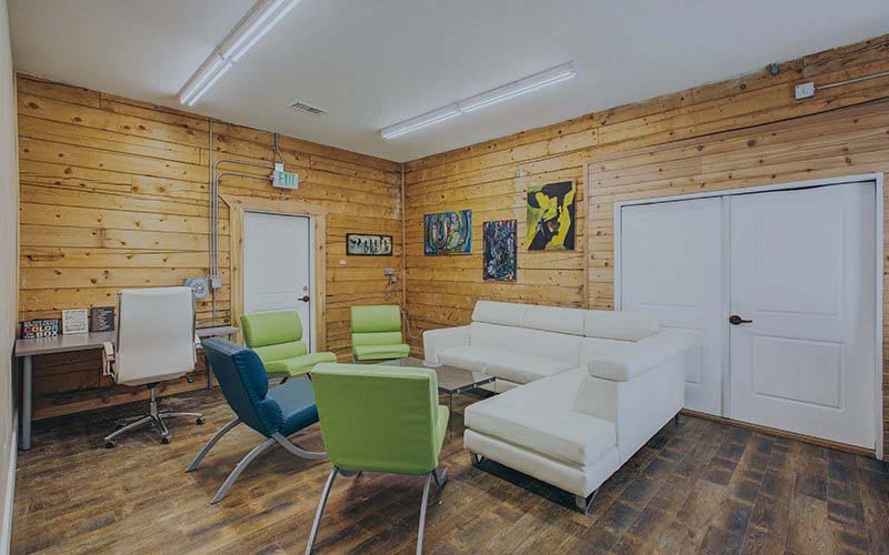 Wooden-walled lounge with white sofas and green chairs.