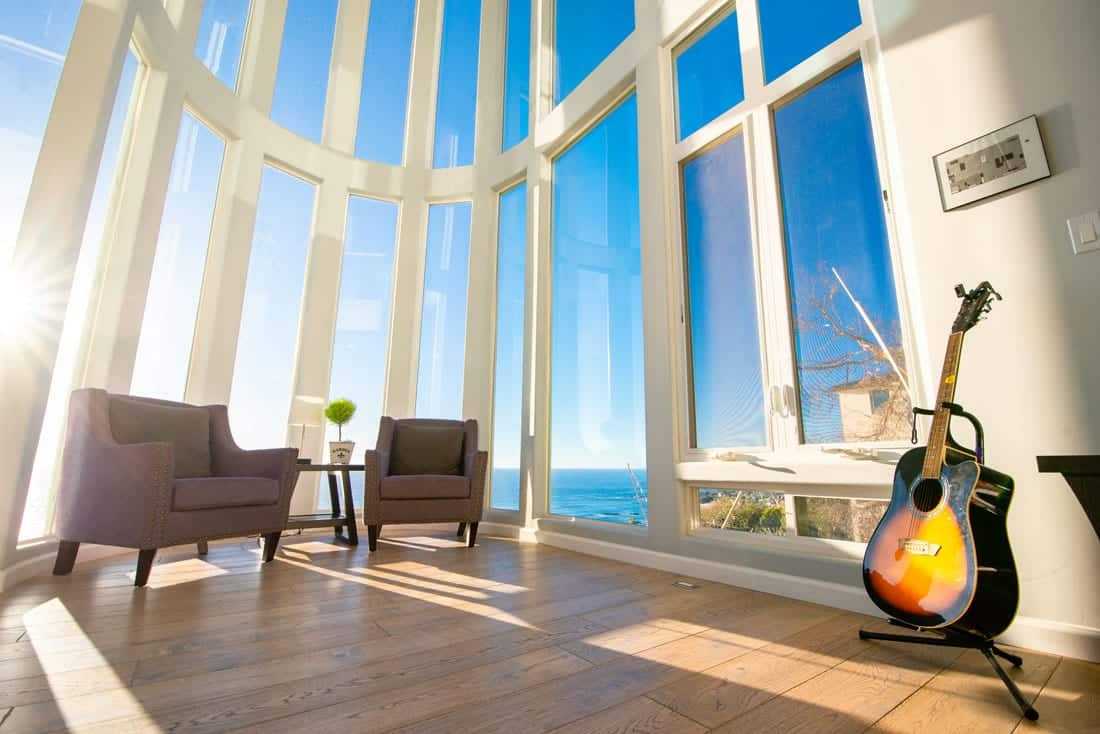 Guitar beside chairs by tall windows with ocean view
