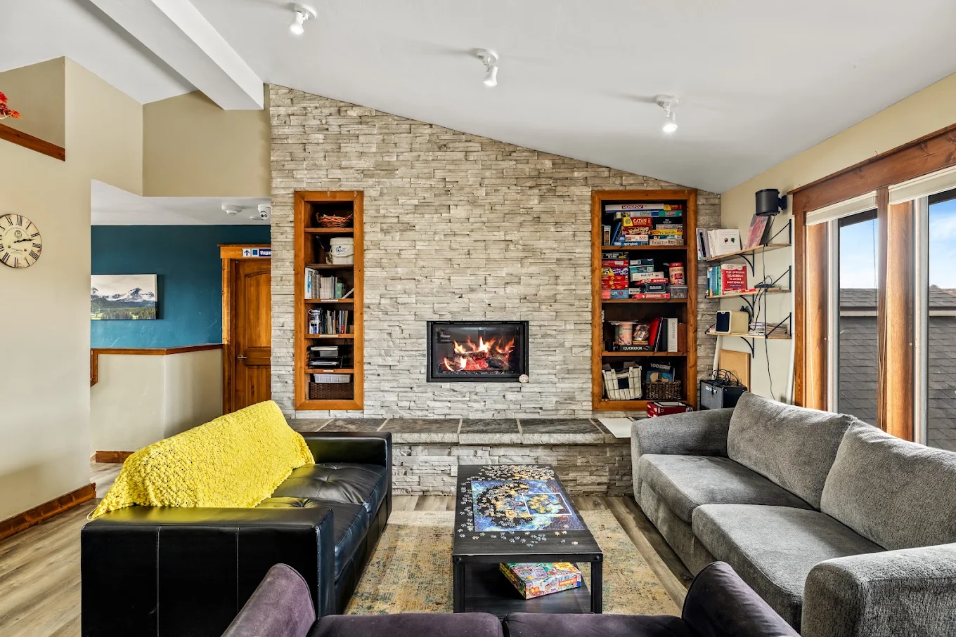Comfortable lounge with sofas, a stone fireplace, bookshelves, games, and large windows