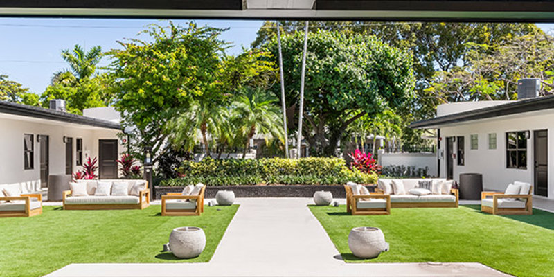  A modern outdoor courtyard with comfortable seating, lush greenery, and shaded areas, offering a peaceful and inviting space for relaxation.