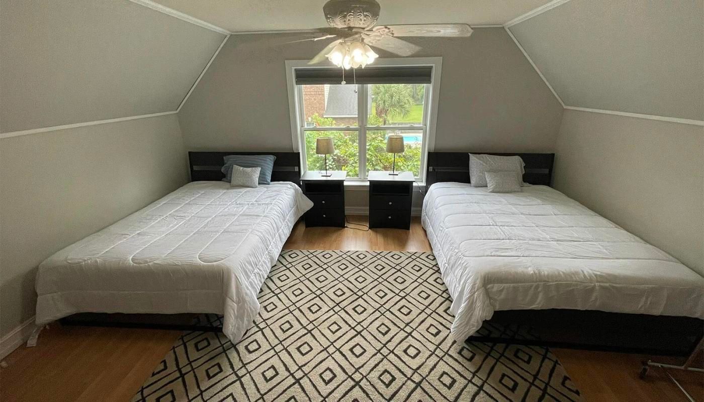 A bedroom with two beds, a ceiling fan, and a window view
