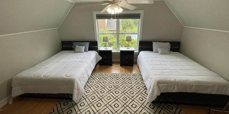 A bright, cozy bedroom with two neatly made beds, a patterned rug, and large windows offering a serene view, creating a peaceful retreat.