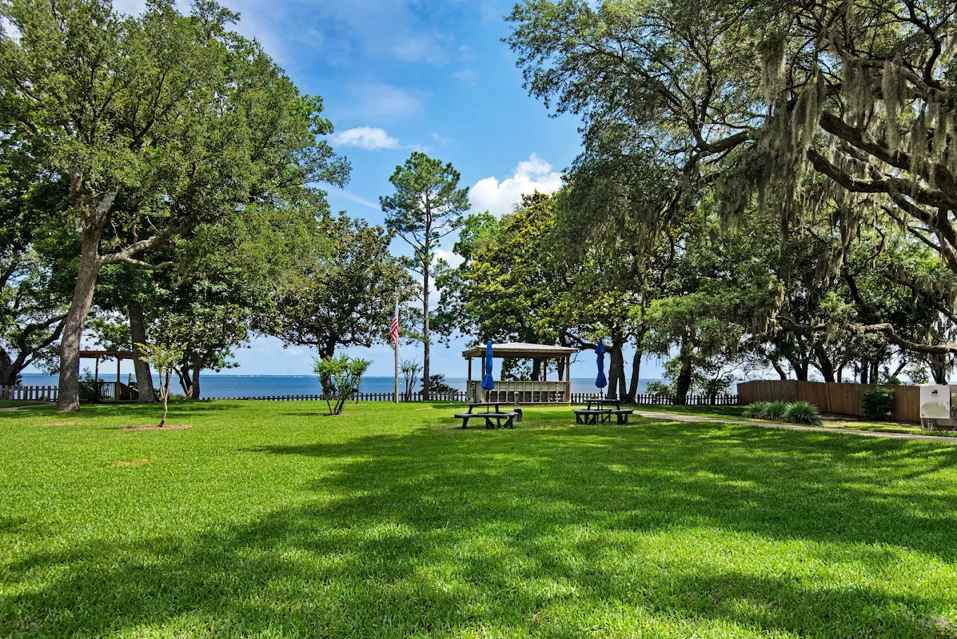 Grassy waterfront lawn with trees, picnic tables, and gazebo
