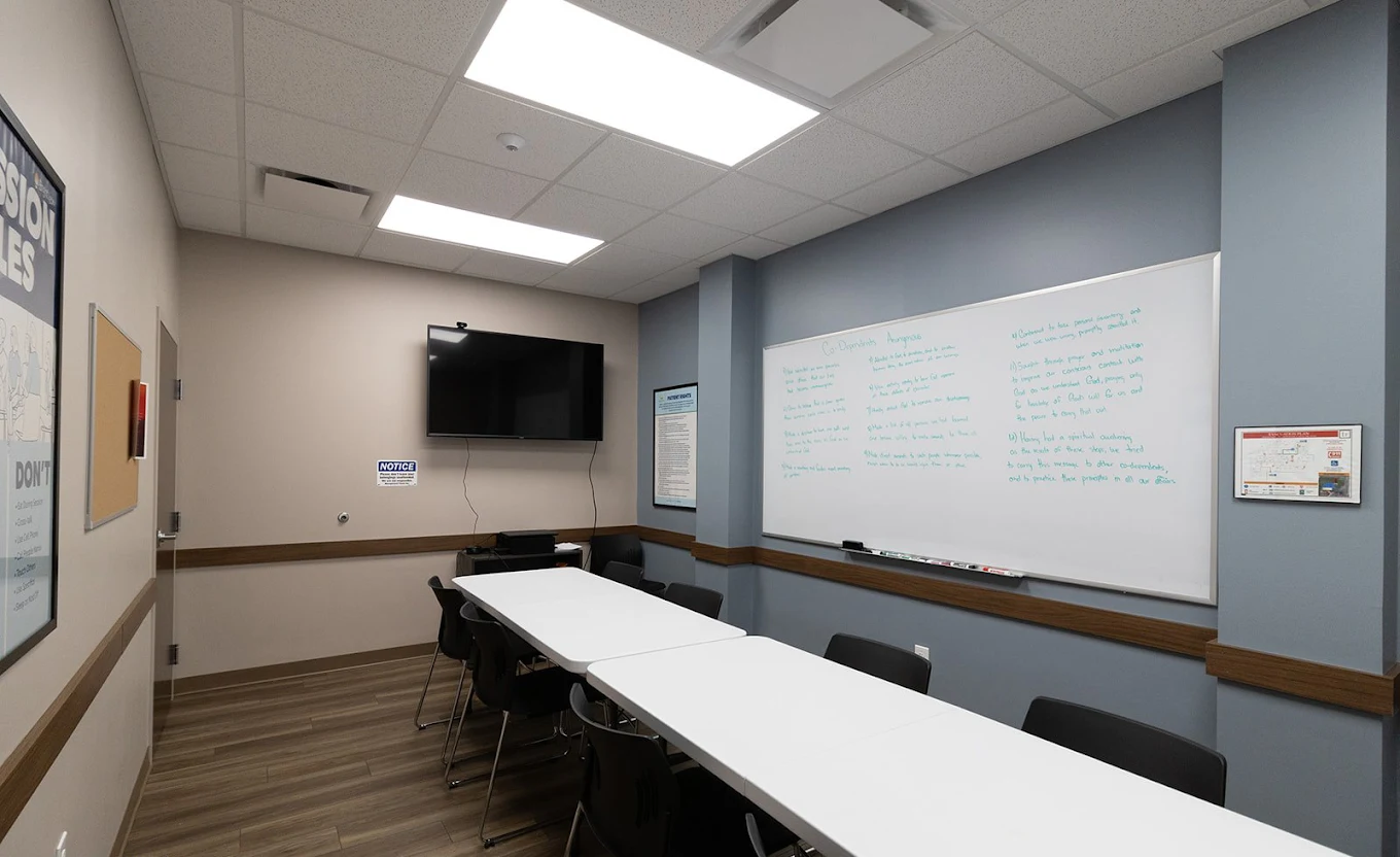 Group counseling room at BrightView Health Kent with white tables, black chairs, a large whiteboard, wall-mounted television, blue accent walls, and wood-look flooring