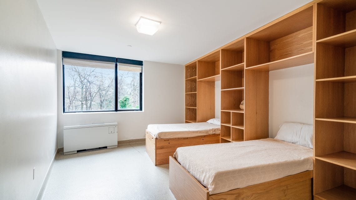 Two beds with built-in wooden shelving and a large window
