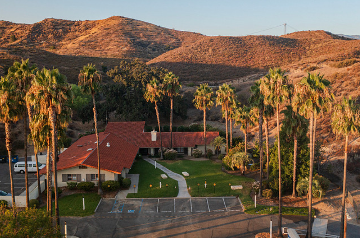 Rehab facility with red roof and palm trees from above.