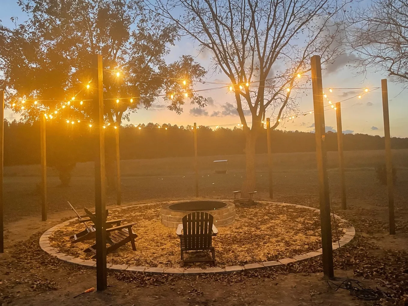 Outdoor fire pit with chairs and string lights at sunset