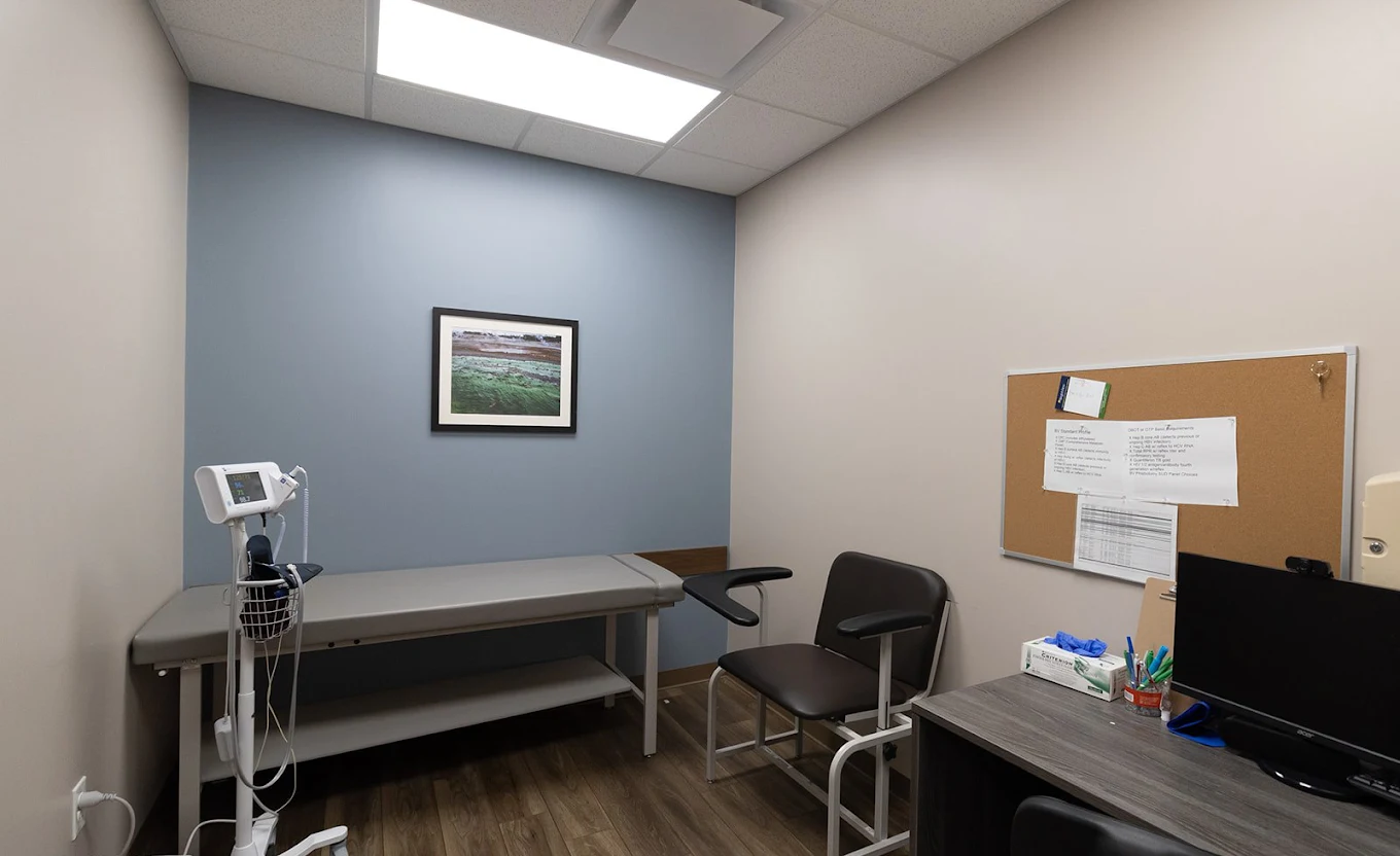 BrightView Health exam room with examination table, vital signs monitor, clinical chair, computer workstation, corkboard, and blue accent wall