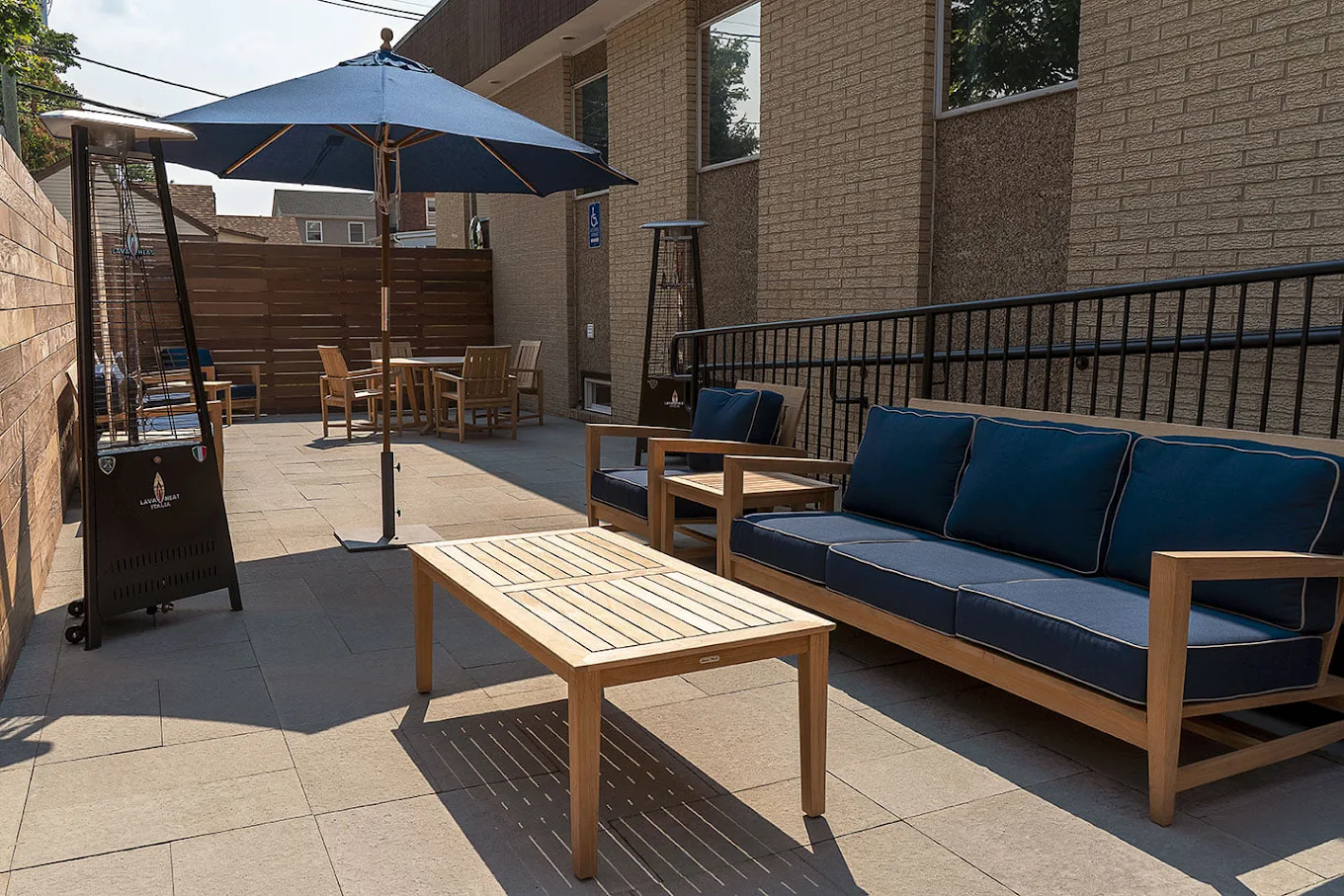 Patio with wooden seating, navy cushions, tables, umbrellas, and heaters