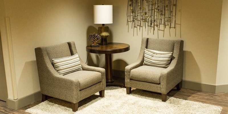 Two cozy armchairs with decorative pillows are placed around a small round table with a warm lamp, creating a welcoming and intimate space.