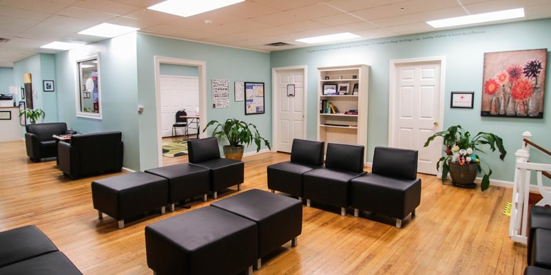 A welcoming lounge area with black modular seating, hardwood floors, soft green walls, and decorative plants, creating a cozy and inviting environment.