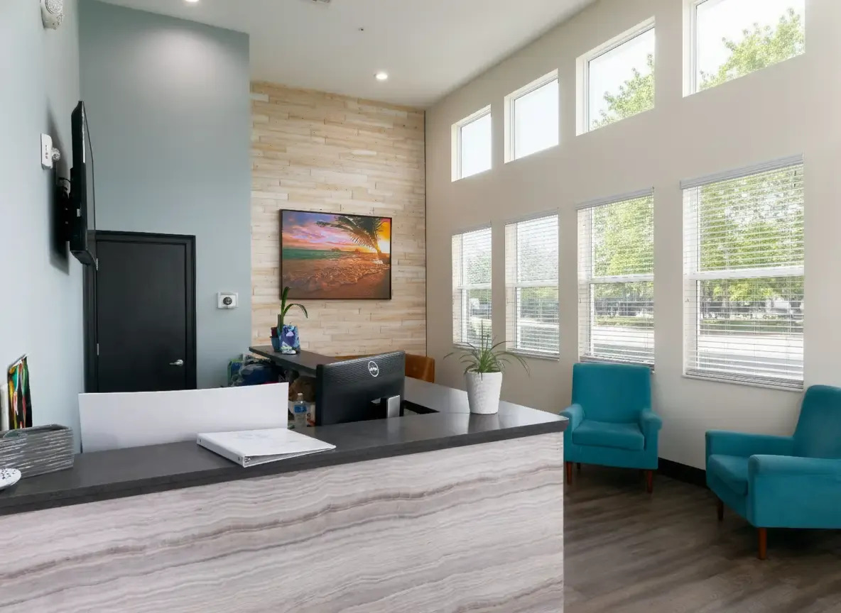 Bright lobby with reception desk and teal seating chairs.