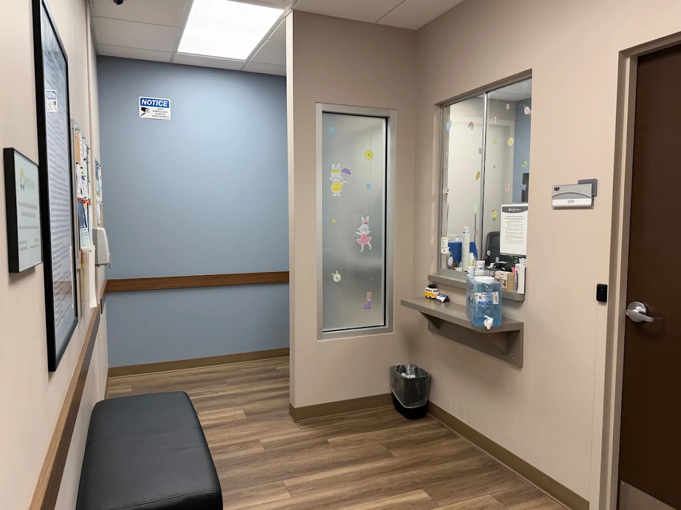 BrightView Health OTP dispensing area with service window and counter, frosted interior window, bench seating, hand sanitizer dispenser, and clinic signage