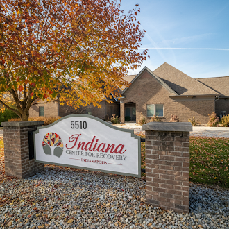 Facility sign in front of brick building with fall leaves.
